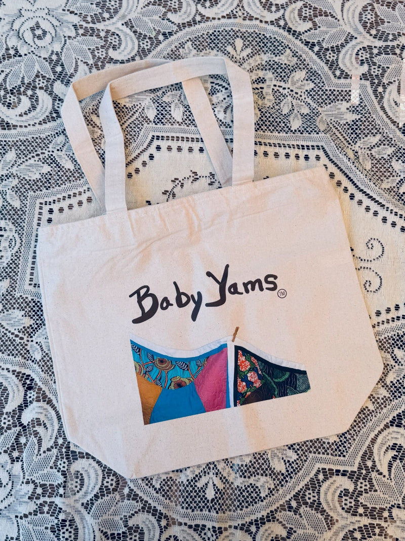 Tote bag with 'Baby Yams' logo on a patterned fabric background
