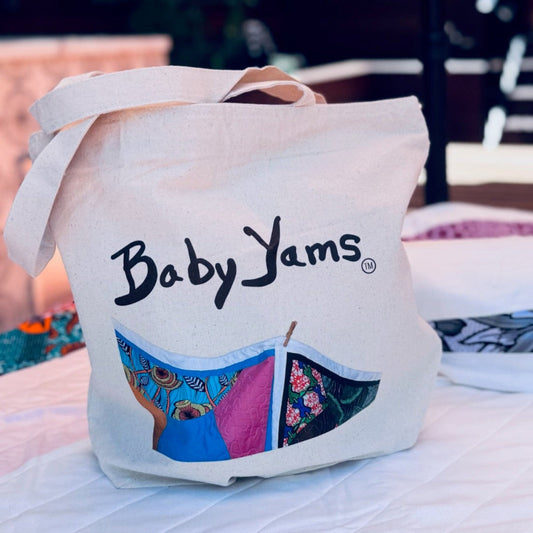 Tote bag with 'Baby Yams' branding on a table with colorful fabric